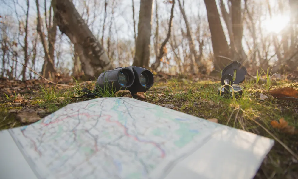 Landkarte und Fernglas liegen auf dem Waldboden